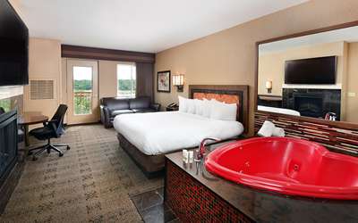 an overview of inside the Honeymoon Suite. Consists of bed, desk, tv, mirror, and heart-shaped tub.